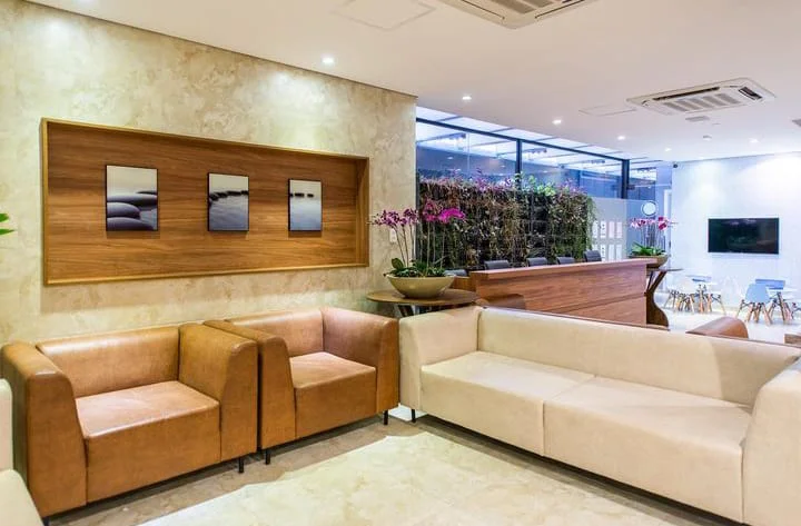 Recepção da clínica com sofás claros, poltronas de couro e orquídeas